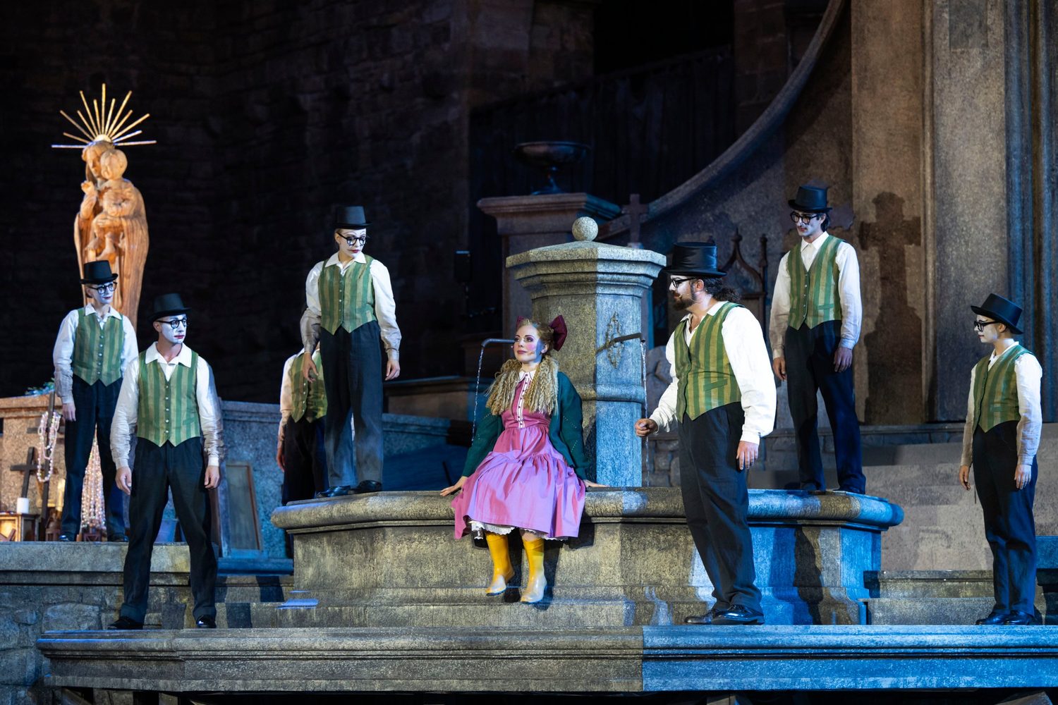 Alexandra Yangel seated on the rim of a fountain, surrounded by men in striped waistcoats and top hats