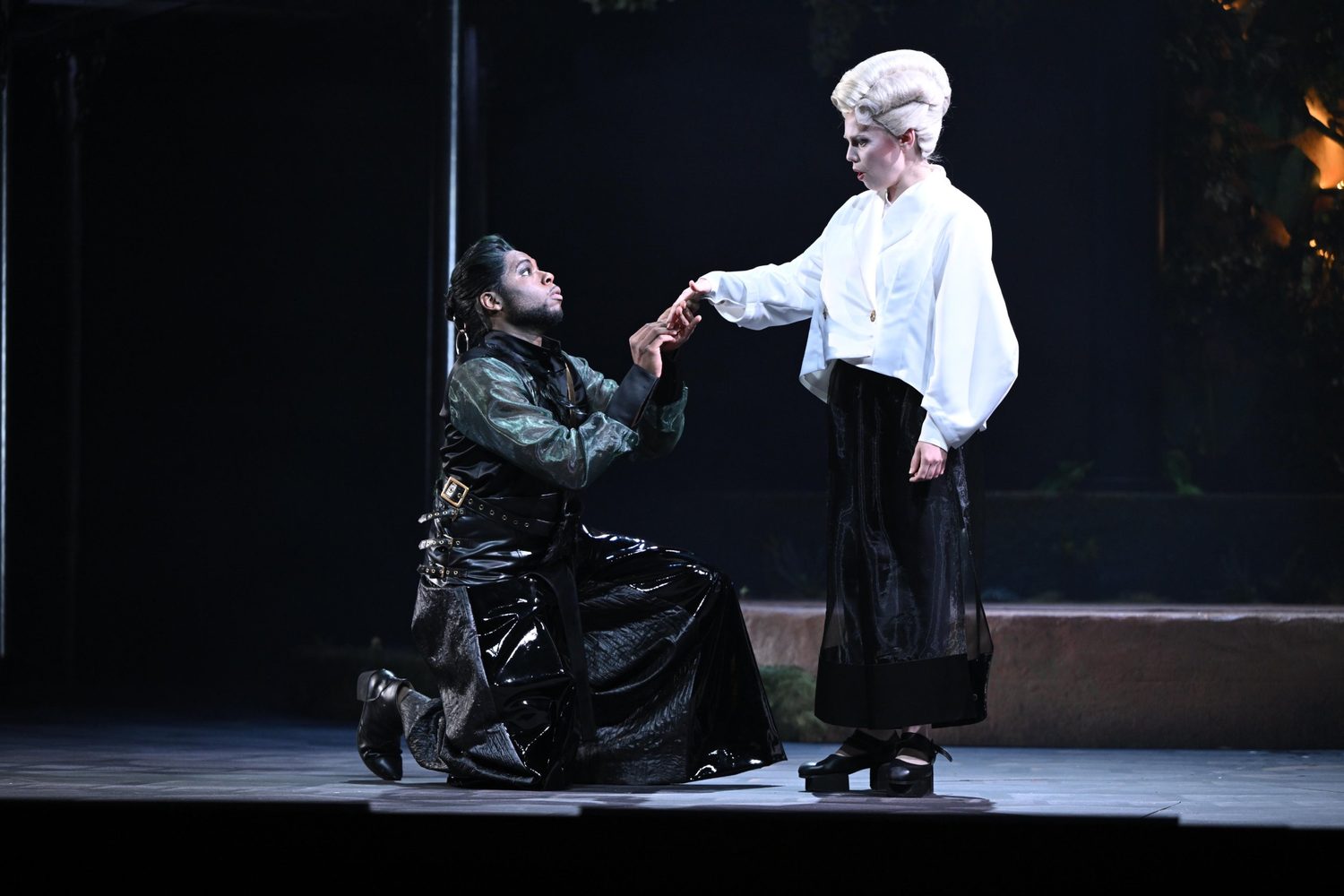 Alexandra Yangel giving her hand to a man kneeling before her on a darkened stage