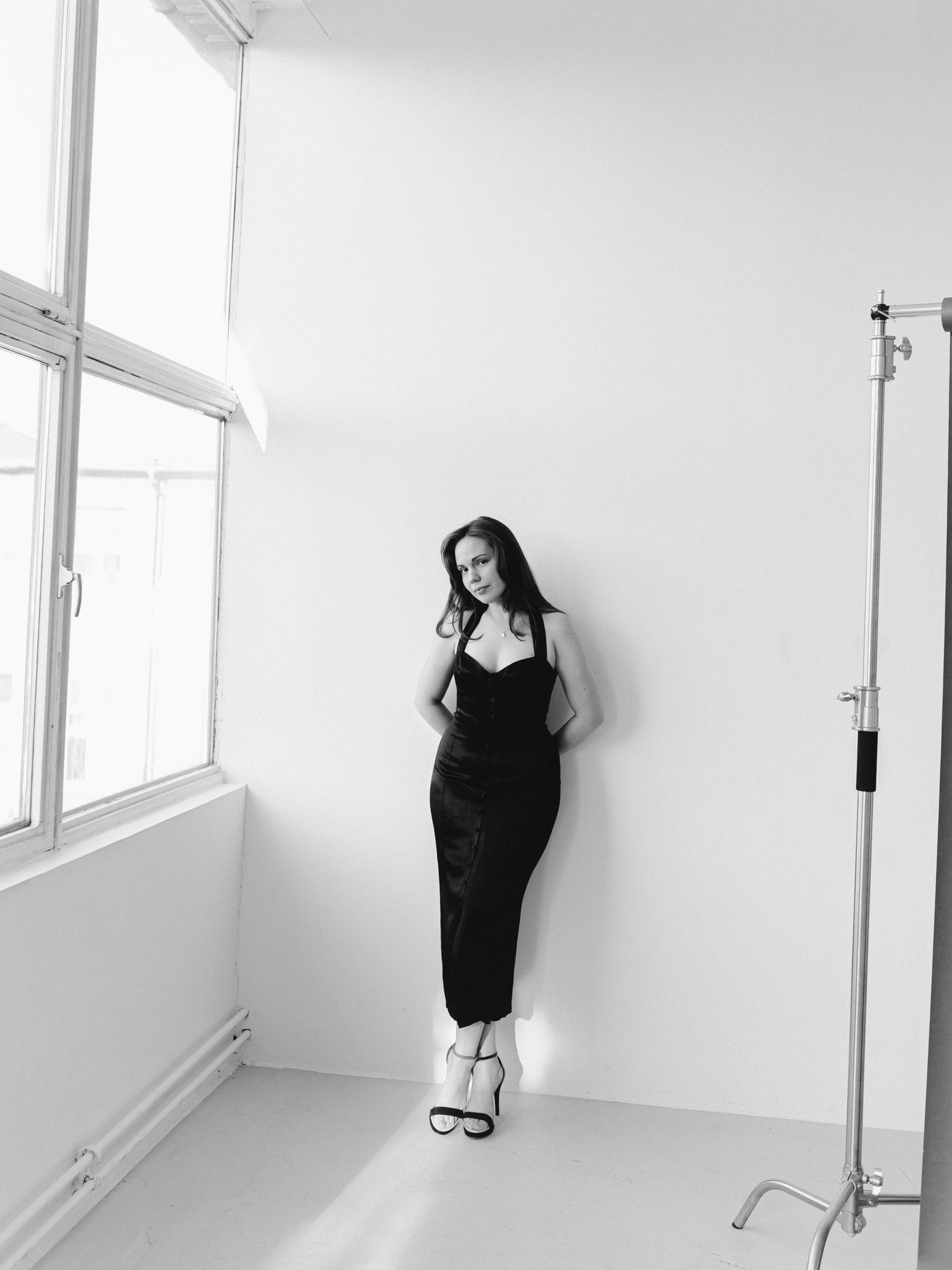 Alexandra Yangel standing against a white wall beside a studio window