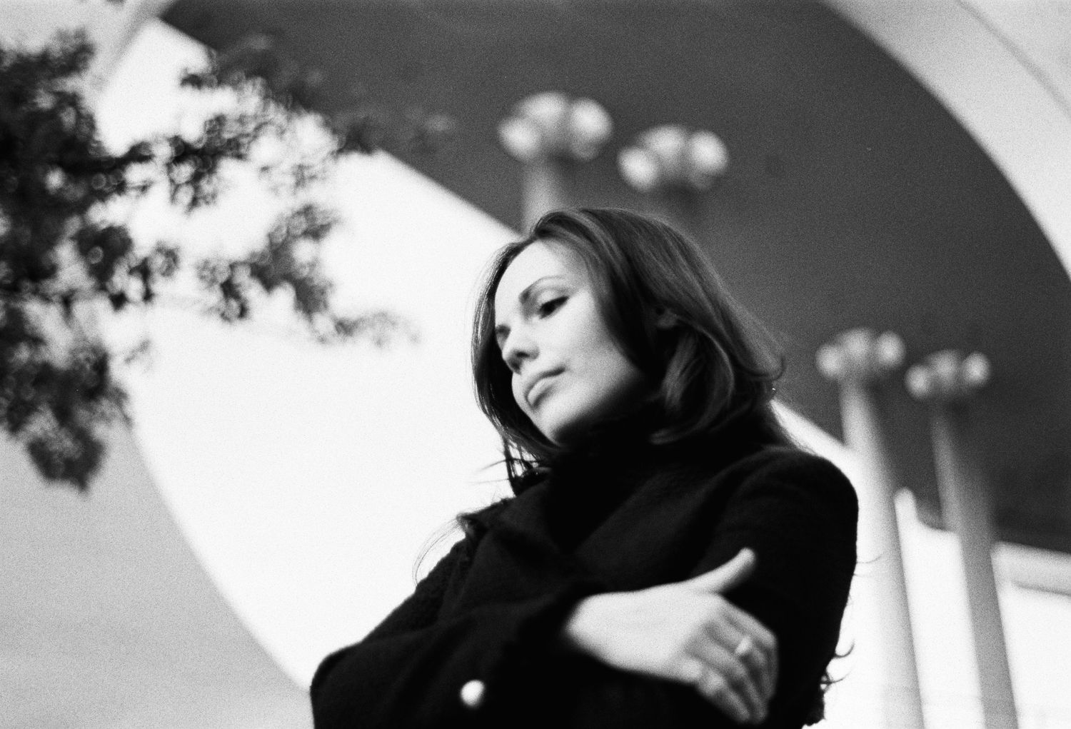 Alexandra Yangel in a dark coat, her arms folded, beneath a curved concrete canopy