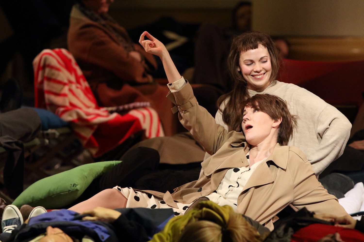 Alexandra Yangel, smiling, cradling another singer who lies back across her lap among a crowd on the floor